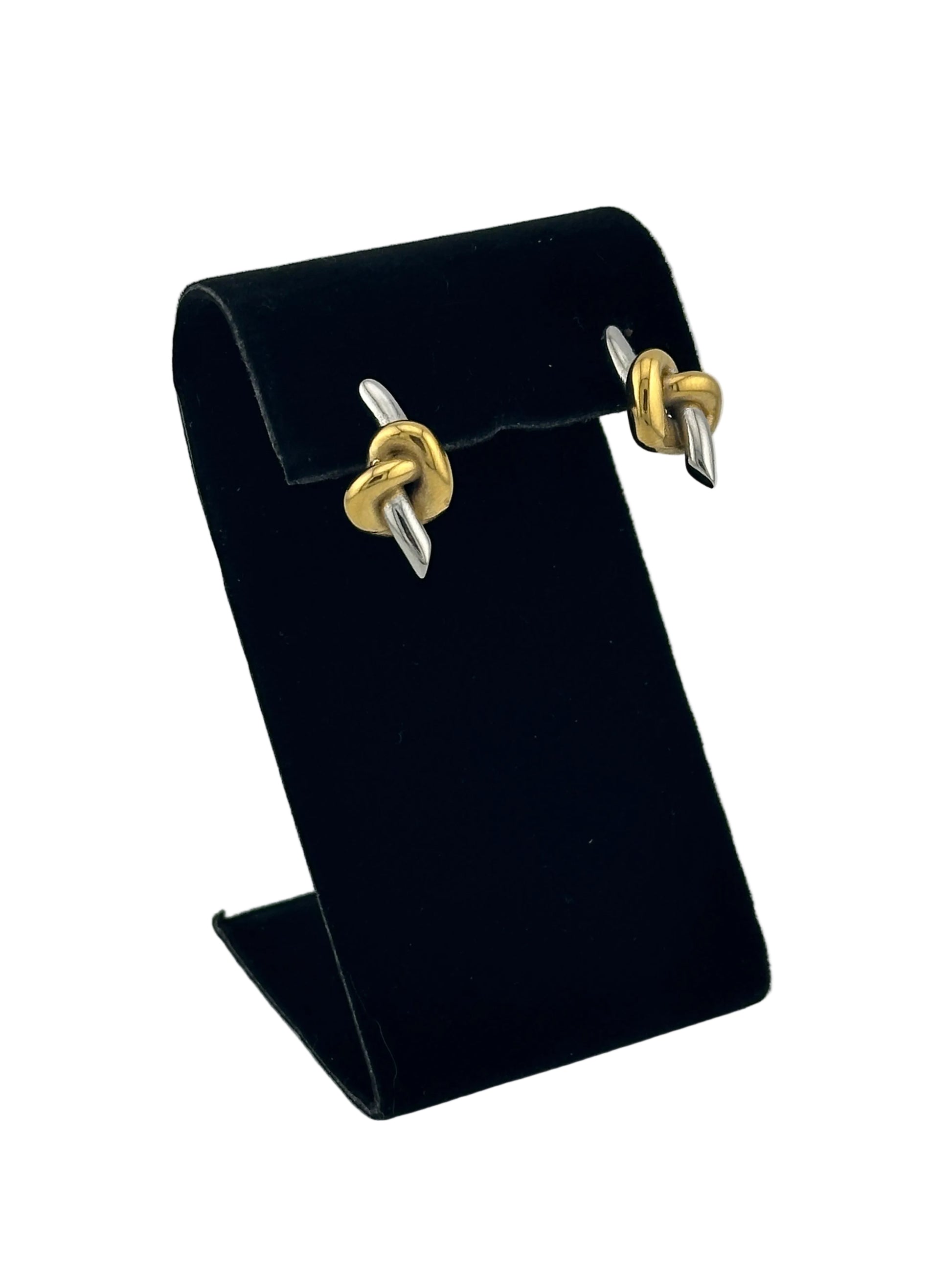 A black velvet jewelry display stand holding a pair of gold and silver knot stud earrings, photographed on a light gray background.