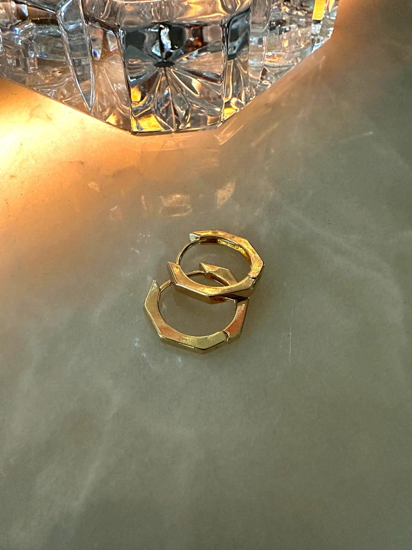 The Elara Geometric Hexagon Clicker Hoops, shown on white marble, with crystal decanter in background