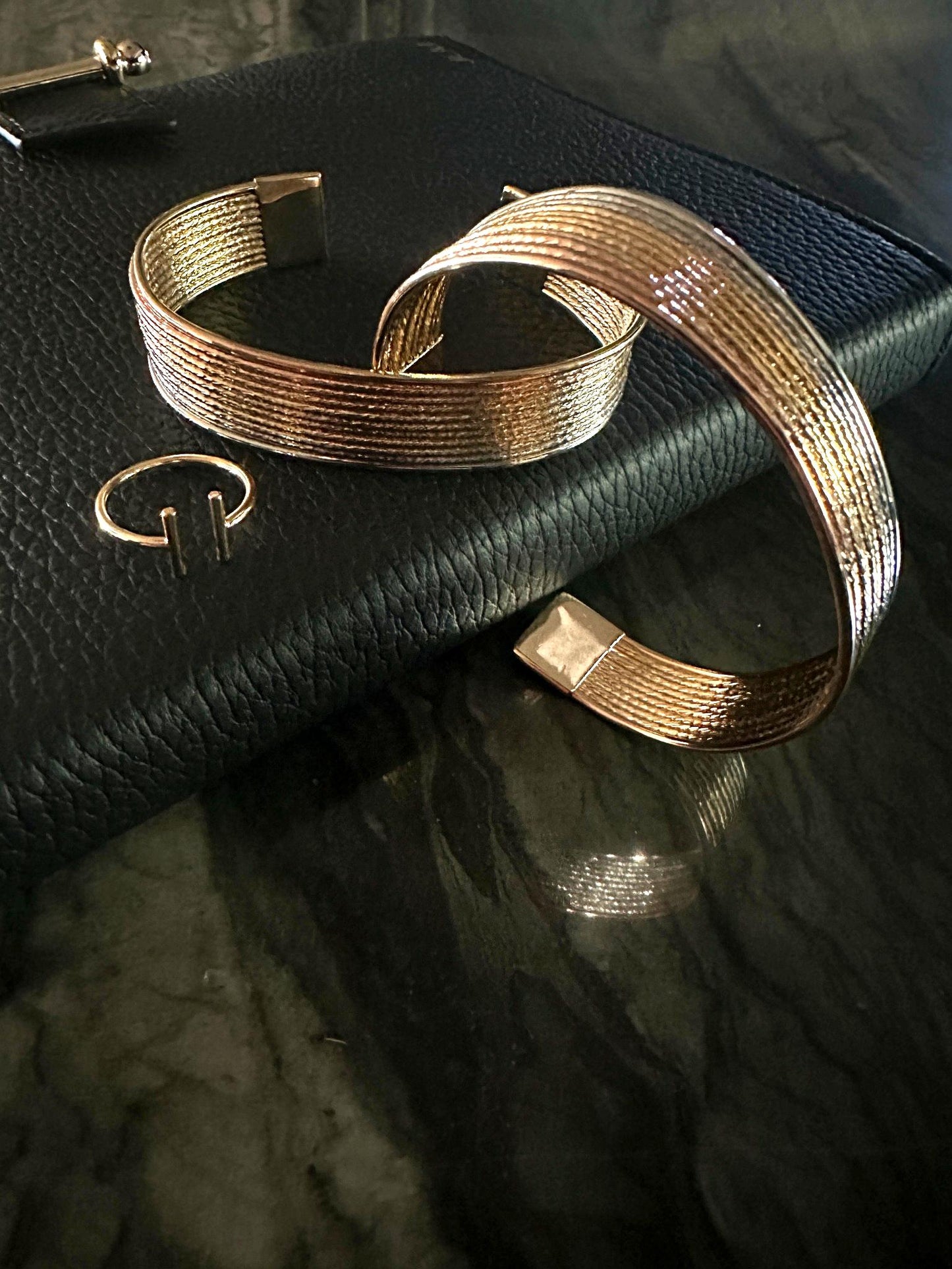 The Eva Parallel Adjustable Ring shown with The Siena Diamond-Cut Tri-Tone Stackable Cuff Bracelets on leather journal and natural stone background