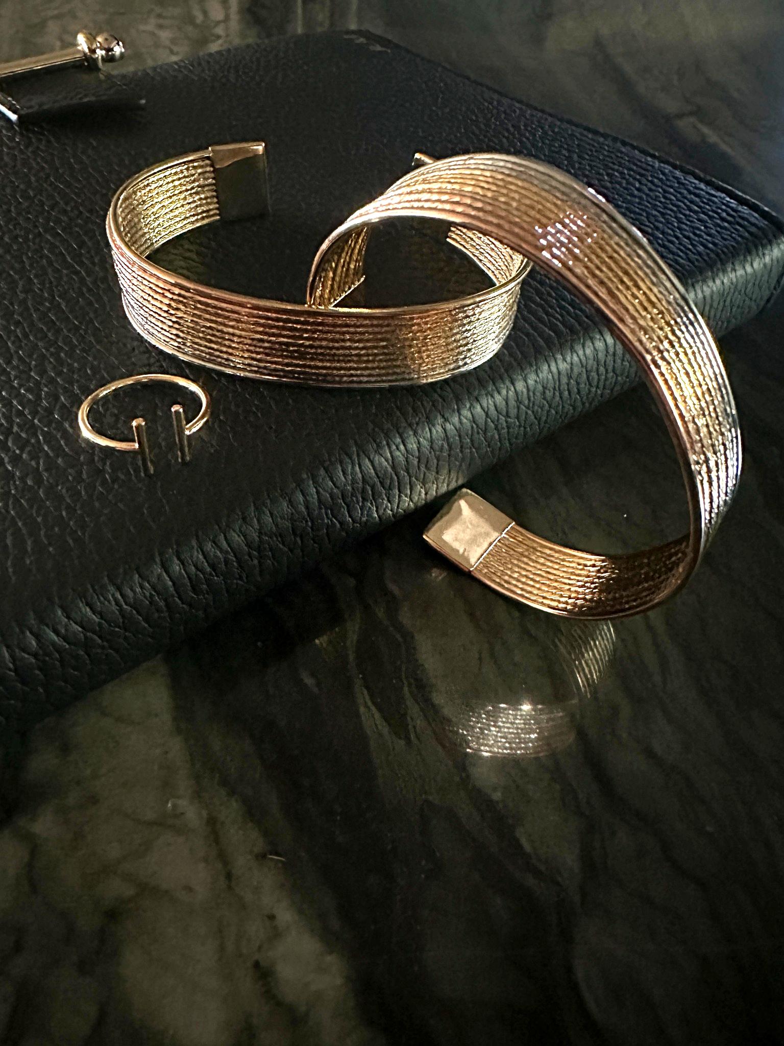 The Eva Parallel Adjustable Ring shown with The Siena Diamond-Cut Tri-Tone Stackable Cuff Bracelets on leather journal and natural stone background