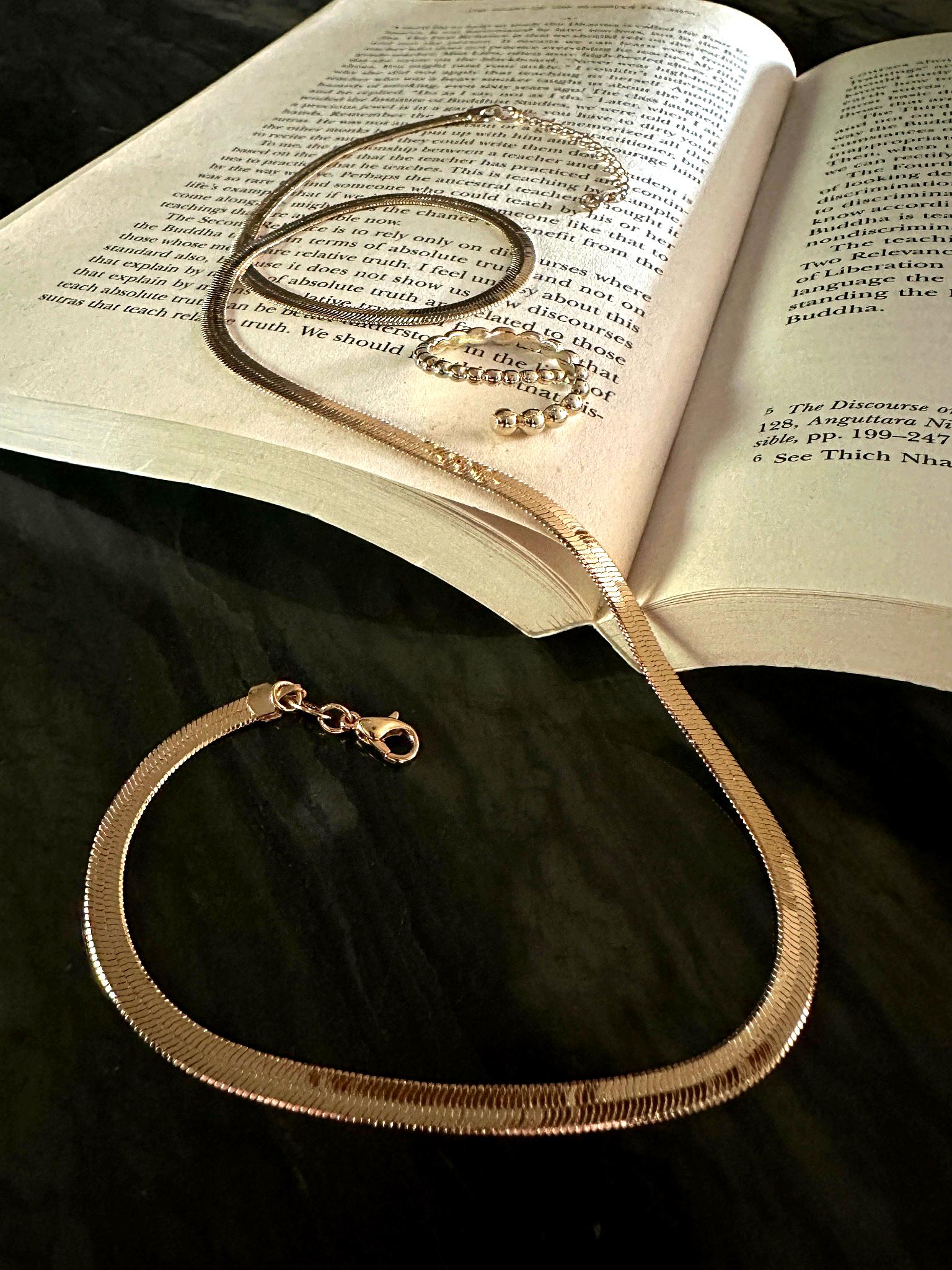 The Capri 4mm Herringbone Necklace and The Noemi Beaded Spiral Adjustable Ring showcased on book and stone background